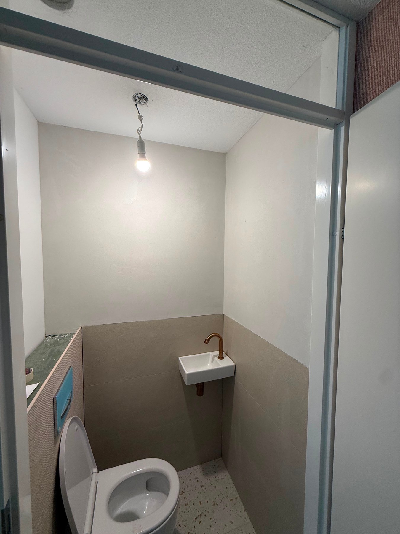Dezelfde toiletruimte na het stucwerk, met gladde lichte wanden, een fonteintje en een koperen kraan