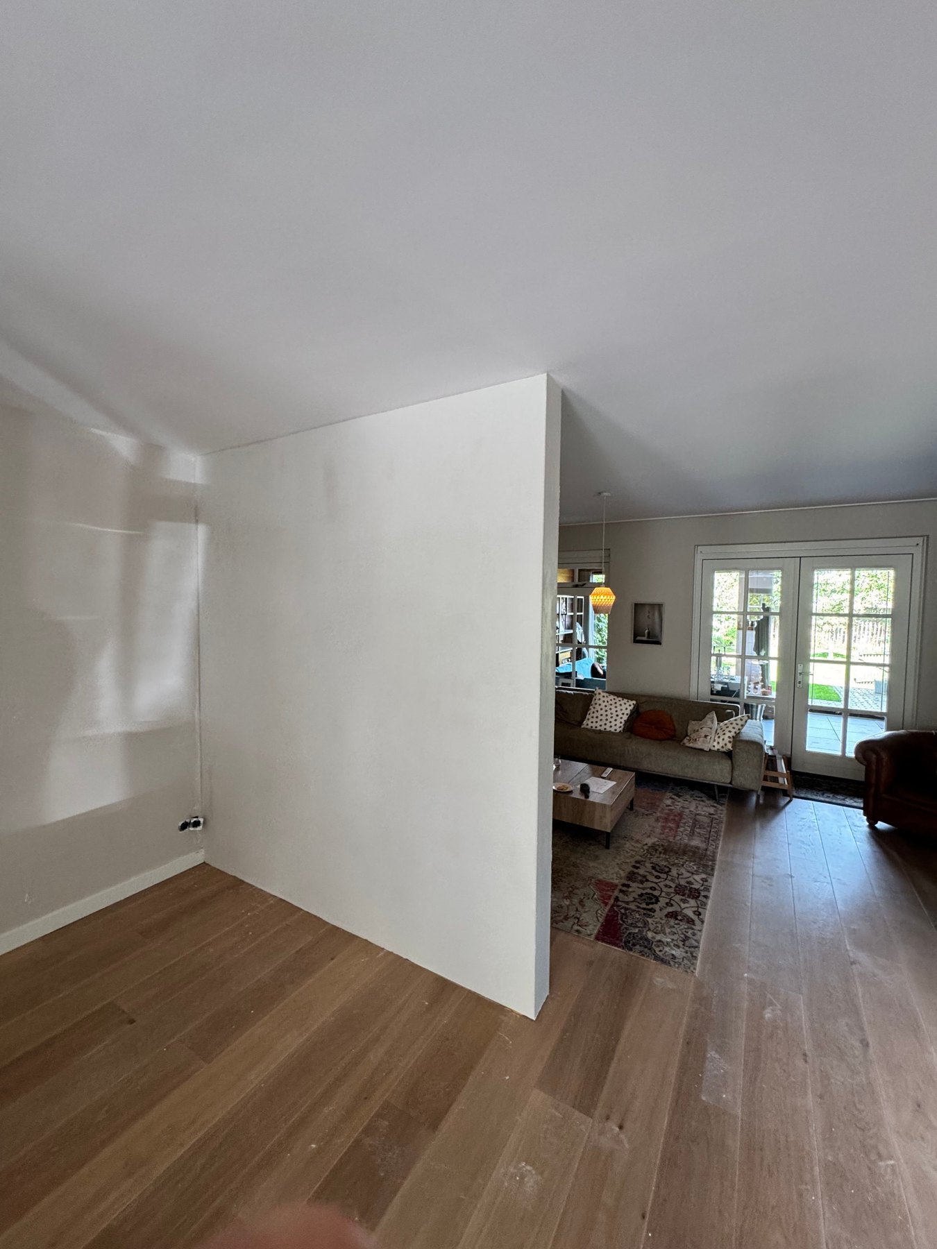 Strak gestucte witte wand met doorkijk naar een woonkamer met eiken vloer